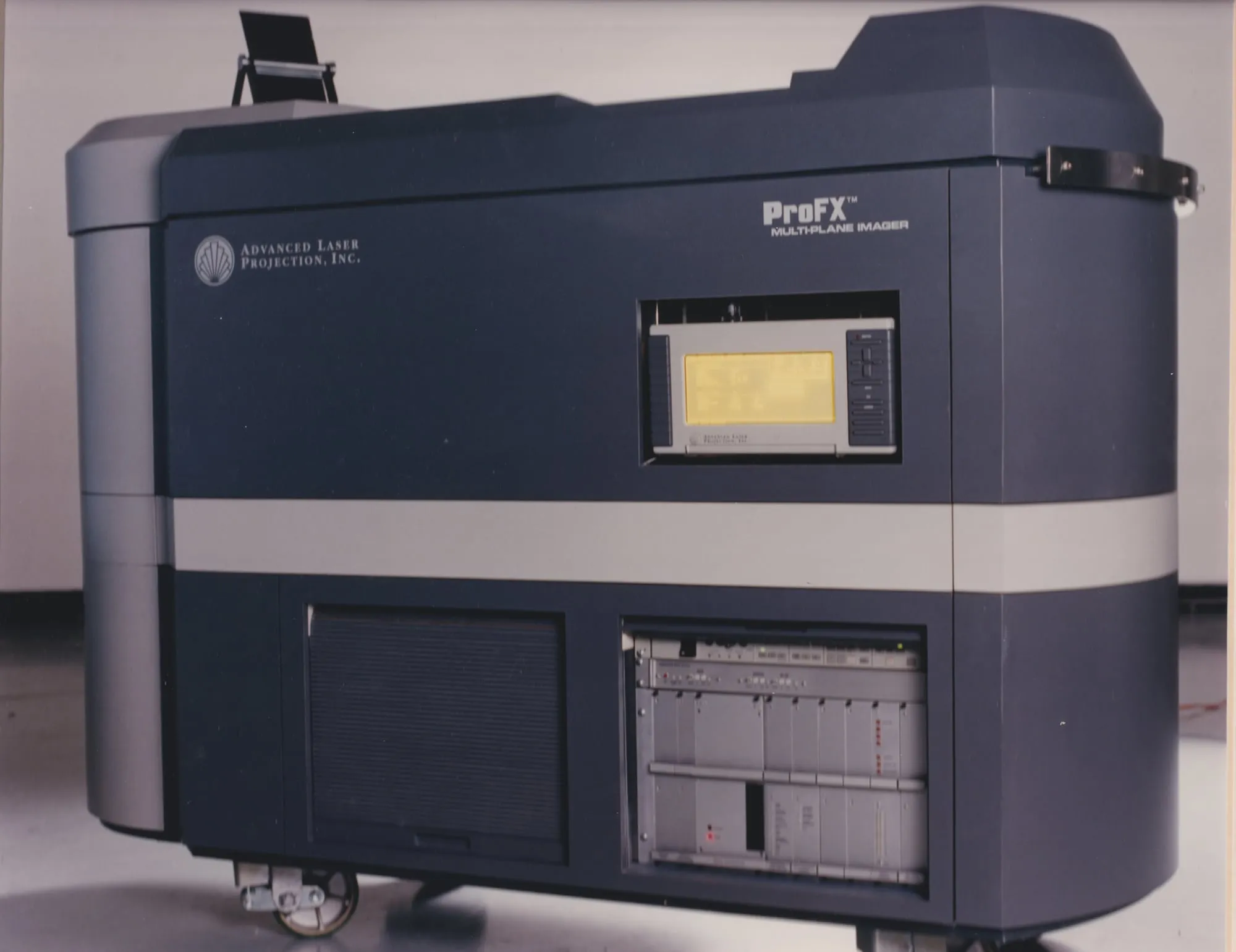The ProFX Multi-Plane Imager by Advanced Laser Projection, Inc. — a large wheeled laser video projector in a navy and grey cabinet, with a lit control panel and an electronics rack visible through the front.