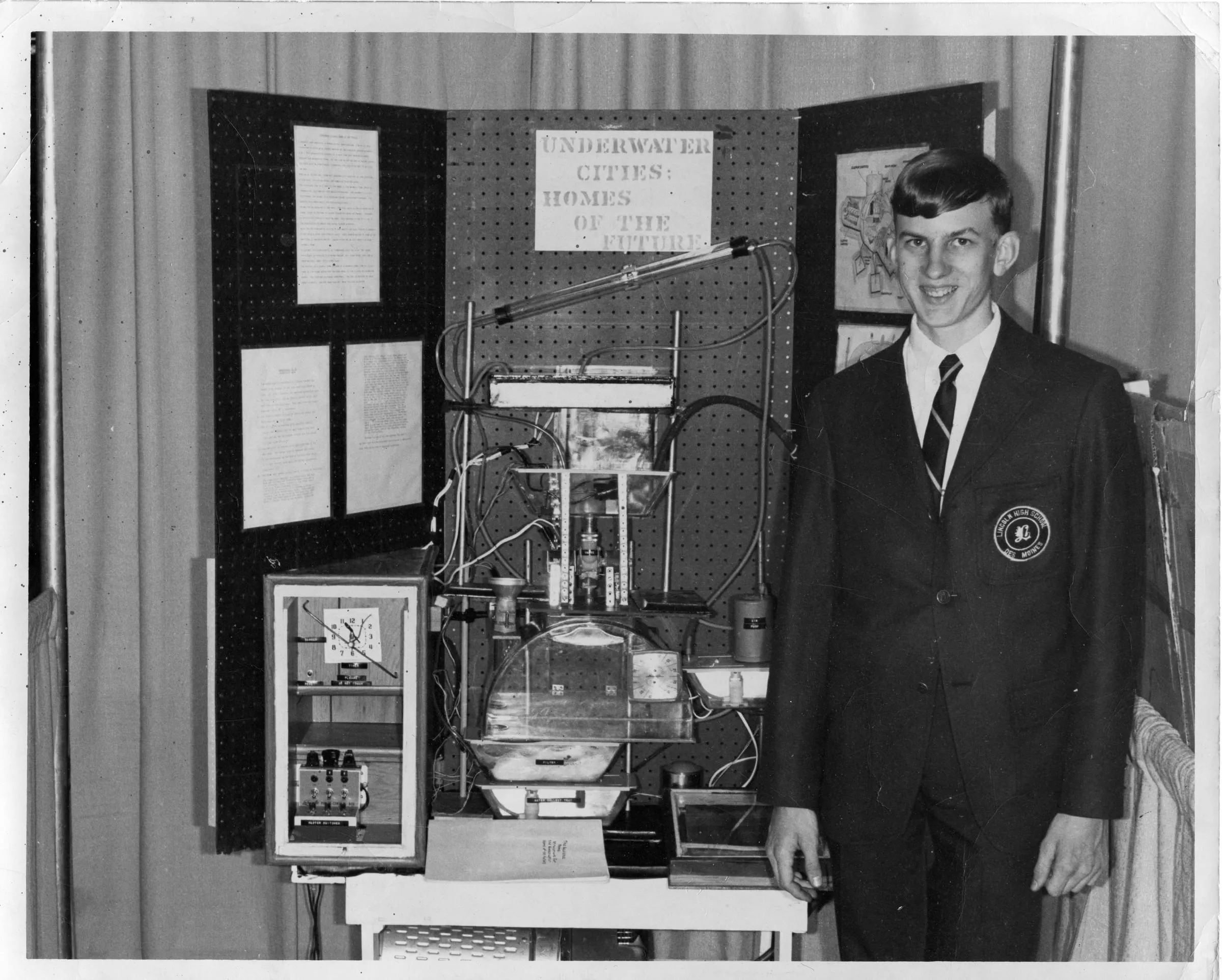 A teenage Paul Linden in a school blazer stands beside his 1968 science-fair project, "Underwater Cities: Homes of the Future."